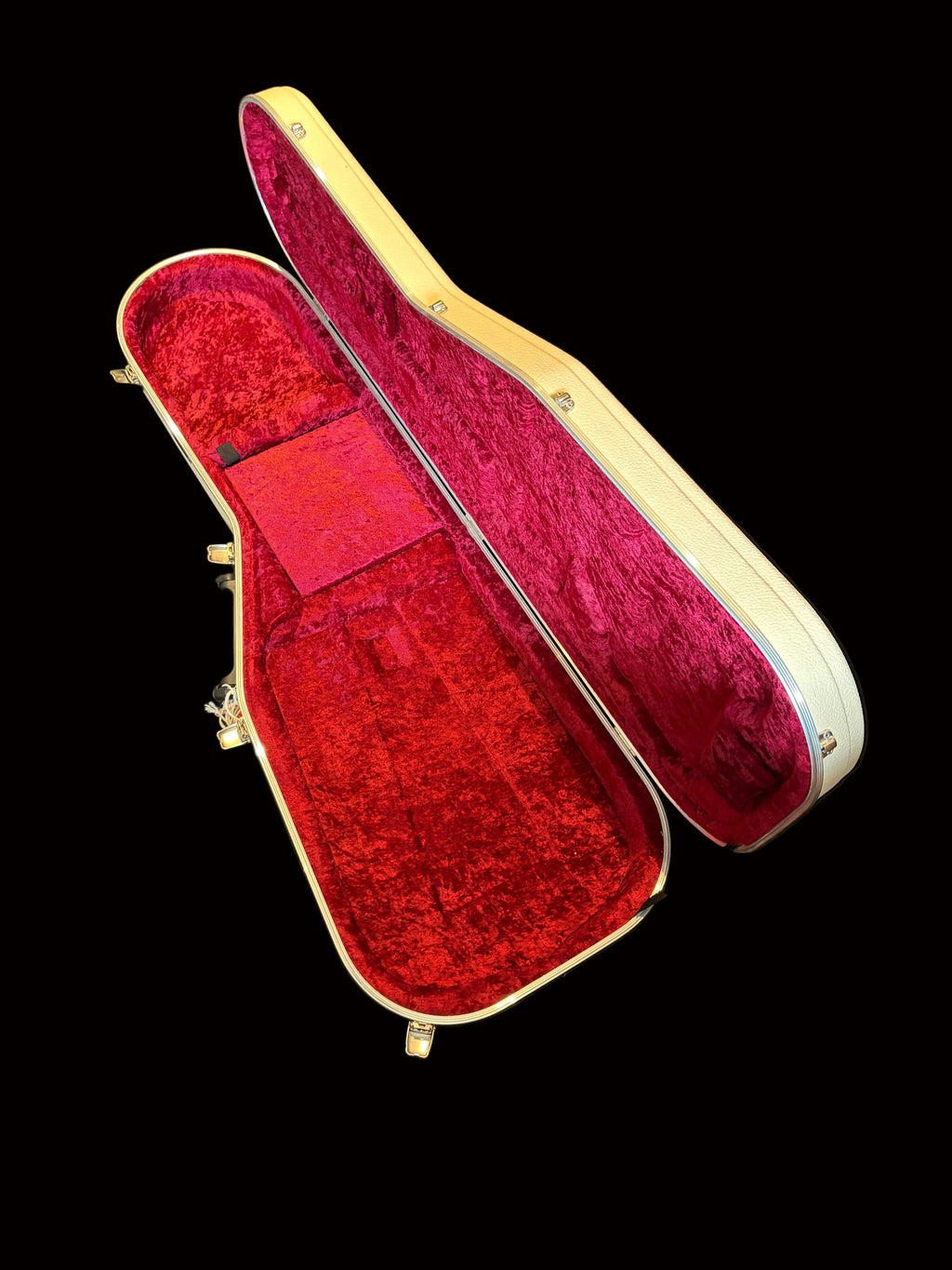 An open hard guitar or instrument case with a cream-colored exterior and plush red velvet interior lining, photographed on a dark fabric surface.